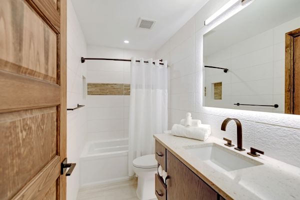 The image shows a clean, modern bathroom featuring a bathtub with a shower curtain, a white countertop with a sink, and a large mirror above it.