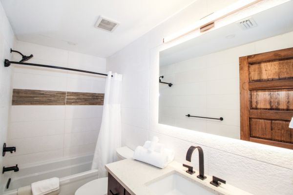 A modern bathroom with a bathtub, a white shower curtain, a large mirror above the sink, and wooden door accents.