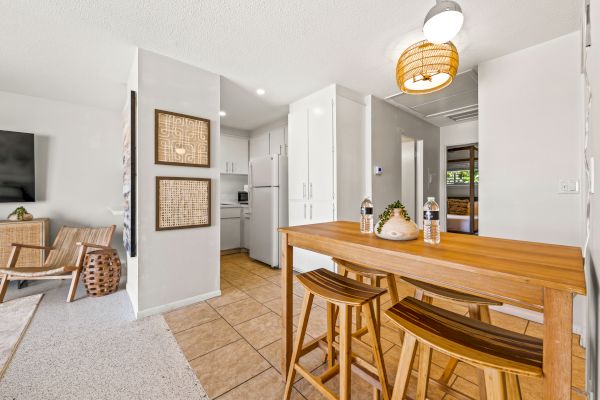 The image shows a modern kitchen and dining area with wooden furniture, decorated wall art, and white cabinets. Cozy and minimalistic design.