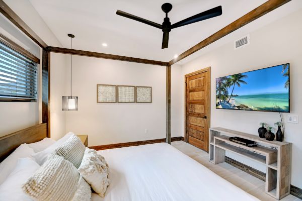 A bedroom with a bed, pillows, a TV on the wall, a ceiling fan, and three framed pictures above the bed.