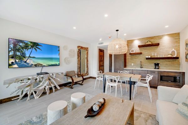 A modern living room features a wall-mounted TV, a unique driftwood console table, a dining area, a small kitchenette, and stylish decor.